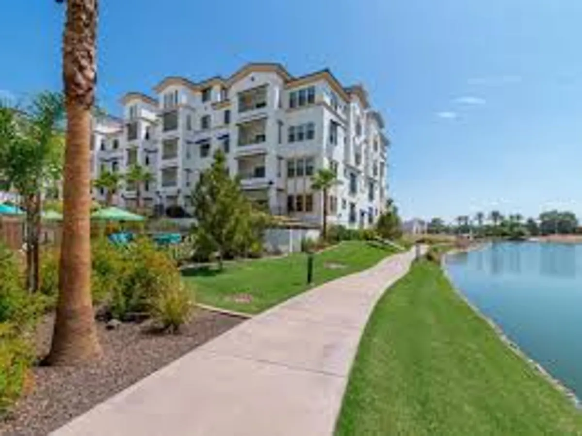 This exterior image presents a modern apartment building surrounded by a lush green lawn and a tranquil lake, with a clear pathway leading toward the water. The scene is peaceful yet inviting, featuring well-designed landscaping and natural elements perfect for relaxation after outdoor activities.