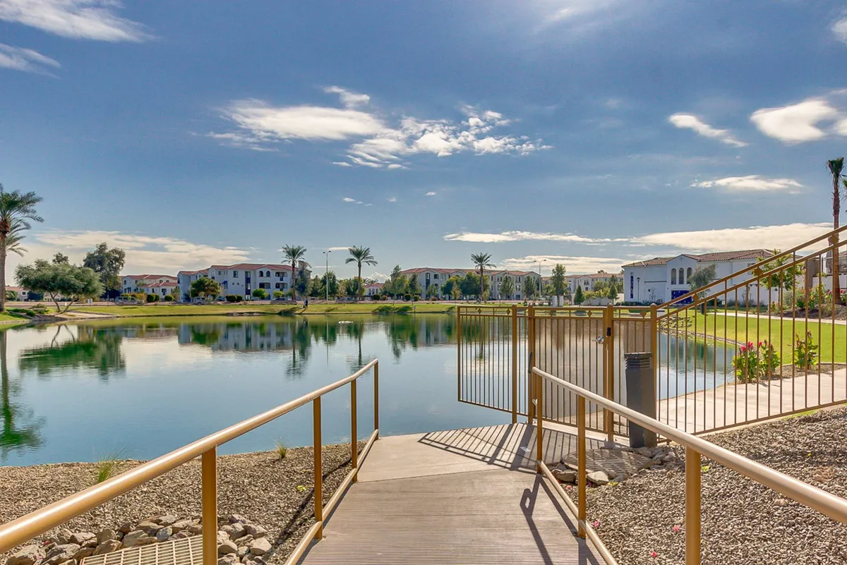 A tranquil view of a calm lake bordered by palm trees and a winding walking path. The area is perfect for leisure strolls, wildlife observation, and peaceful moments by the water, reflecting the scenic trails and outdoor amenities available nearby.