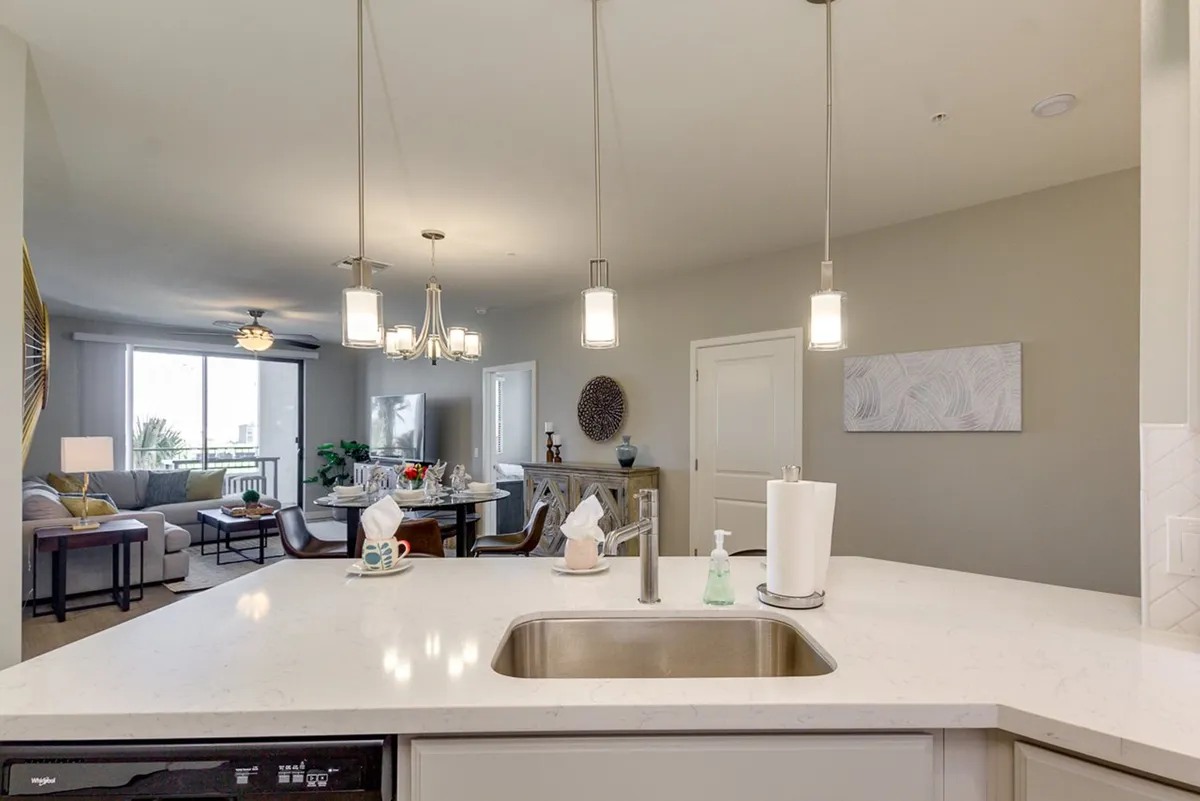 This interior image displays an open-concept living area seamlessly flowing into the kitchen and dining space. The kitchen island, dining table, and adjacent living room are all visible, giving a sense of spaciousness and the interconnectedness of the main social zones. Abundant natural light and tasteful decor create a welcoming and modern atmosphere.
