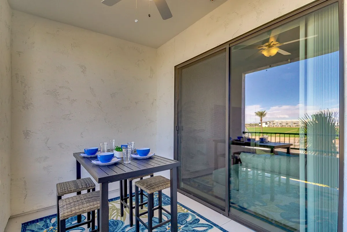 A bright dining area features a table set with blue dishware, positioned near a sliding glass door that opens to outdoor views. The image hints at seamless indoor-outdoor living, perfect for casual brunches, sunset dinners, or entertaining friends against a scenic backdrop.