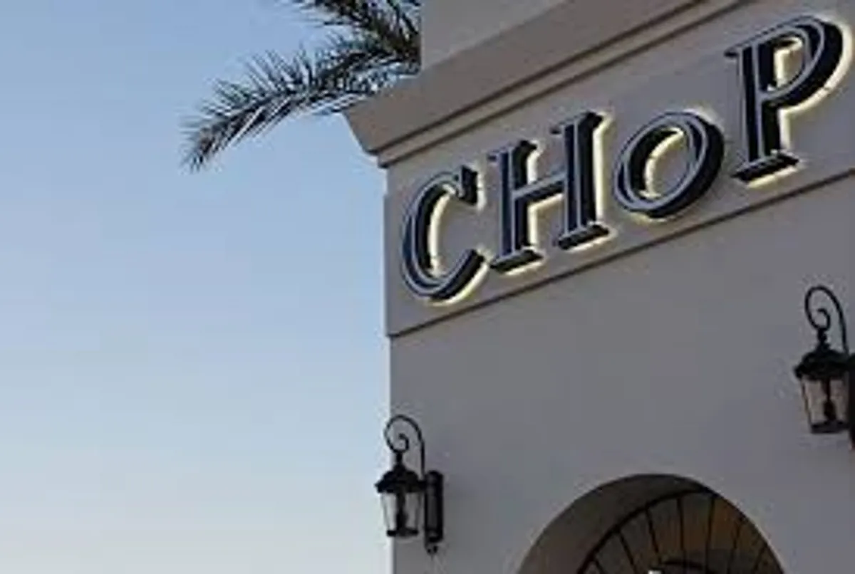 A vibrant exterior scene of a local restaurant with a glowing sign, hanging lanterns, and a palm tree, suggesting nearby dining options. The convivial mood encourages exploration of the local culinary scene, just steps from the residence.