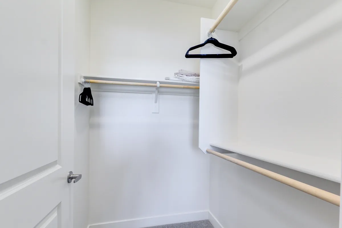 A minimalist walk-in closet with organized hanging space, white walls, and shelving—ready for personal belongings and generous storage needs.