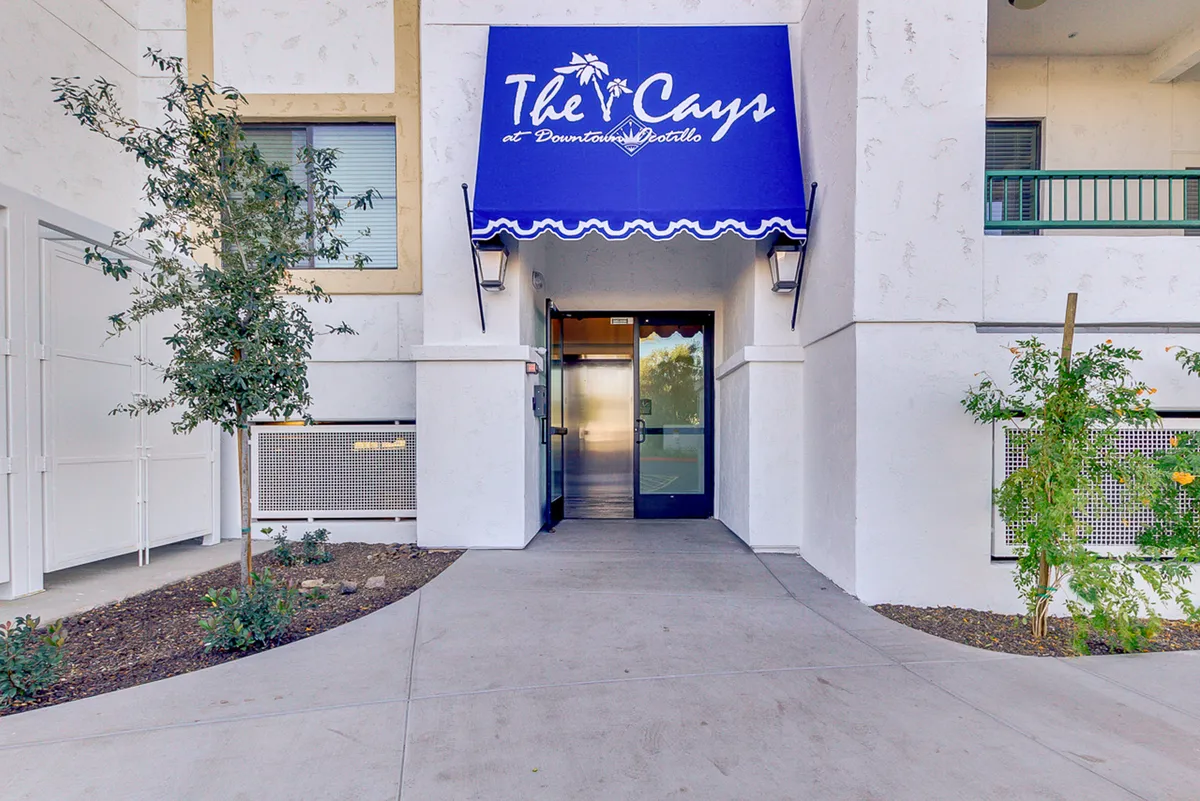 This exterior image highlights the welcoming entrance to the property, complete with an elegant awning, attractive landscaping, and a visible doorway. The scene suggests a friendly, upscale community ambiance ideal for guests arriving or gathering outdoors.