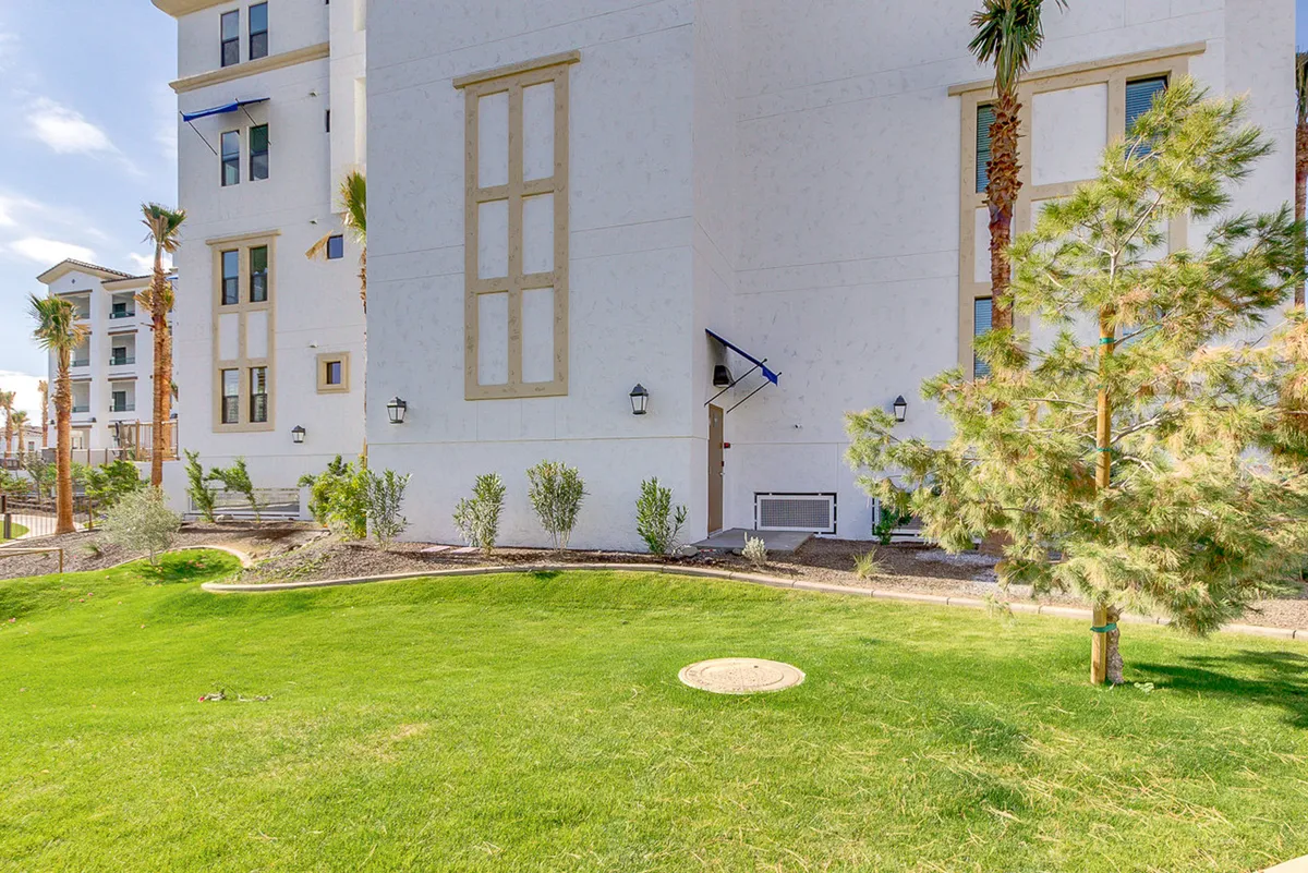 An inviting exterior view featuring a modern building with sleek architecture, palm trees, a well-manicured lawn, and decorative lighting. The scene suggests a vibrant, active environment perfect for outdoor gatherings, walks, or relaxing under the Arizona sun.